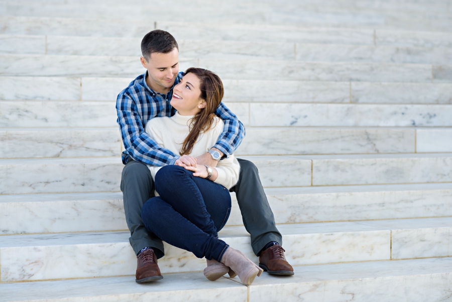 A man making his fiance laugh on the steps of the lincoln memorial.